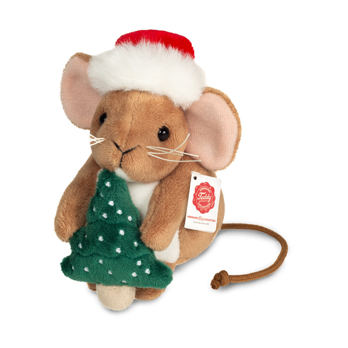 Das ist eine kleine Weihnachtsmaus mit Tannenbaum von Teddy-Hermann. Sie sitzt und hat kurzes, dichtes, leicht glänzendes Fell in Beige, dazu einen weißen Bauch und einen weißen Fleck auf der Brust. Schnauze und Pfoten sind beige, die Pfotenballen ebenso, die Ohreninnenseiten blassrosa. Die Augen sind schwarz und rund, die Nase klein und schwarz mit cremefarbenen Schnurrhaaren. Hinten sitzt ein langer, dünner brauner Schwanz. Sie trägt eine rote Weihnachtsmütze mit weißem Plüschrand und hält einen grün...