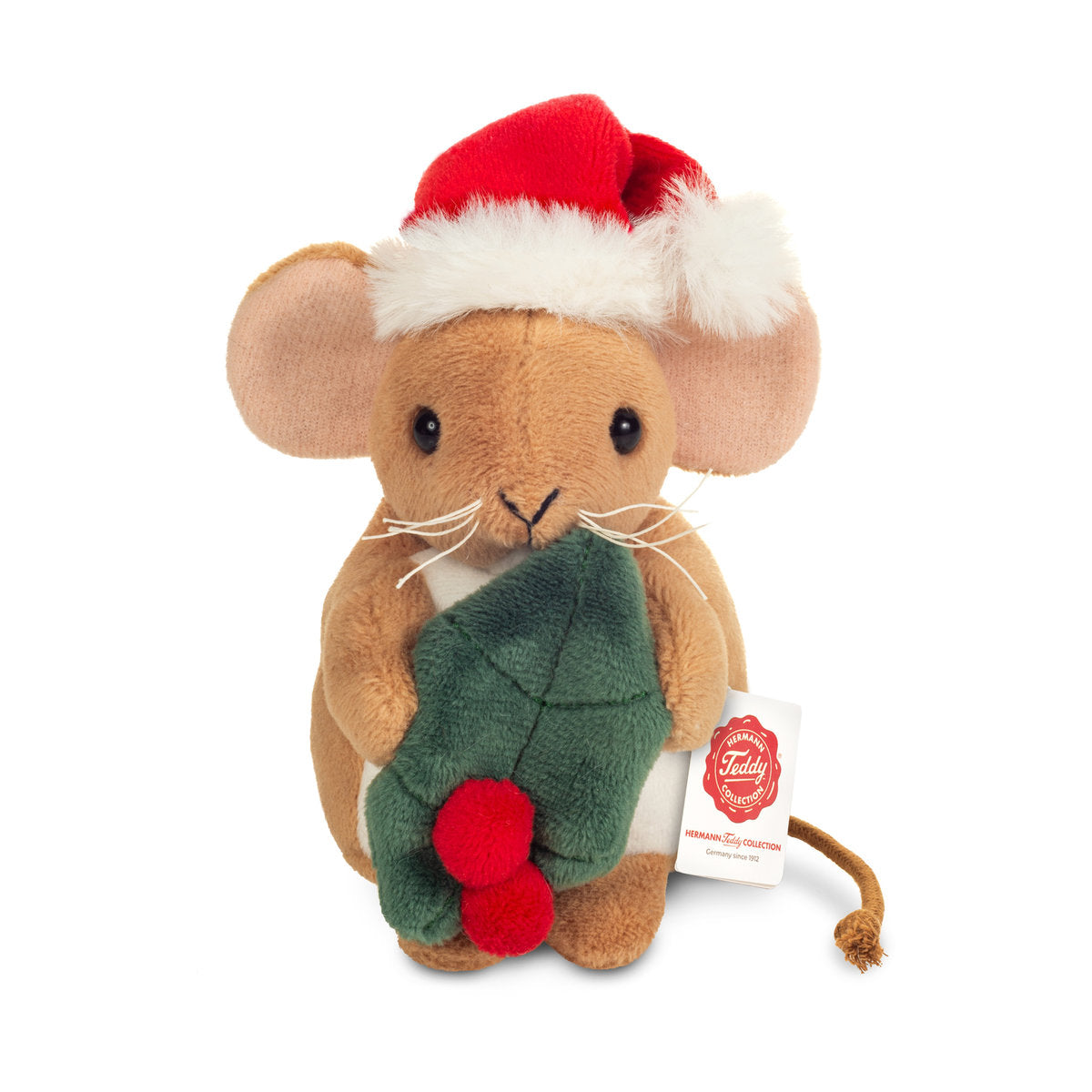 Das ist eine kleine Weihnachtsmaus mit Stechpalme von Teddy-Hermann. Kurzes, glattes, leicht glänzendes beiges Fell, weißer Bauch, blassrosa Ohreninnenseiten. Schwarze runde Augen, kleine schwarze V-förmige Nase, weiße Schnurrhaare. Die Pfoten sind beige, hinten ein dünner brauner Kordelschwanz. Sie sitzt aufrecht, hält ein grünes Stechpalmenblatt mit zwei roten Beeren und trägt eine rote Weihnachtsmütze mit weißem Rand und Bommel. Der Ausdruck wirkt sanft und zufrieden.