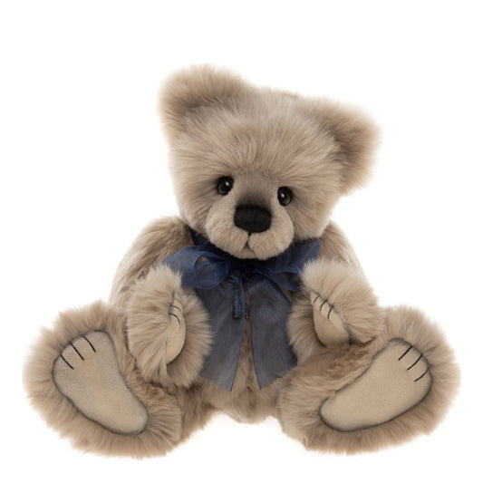Das ist Howarth, ein Teddy von Charlie Bears. Er sitzt und hat langes, dichtes, leicht seidiges Fell in Beige, das in den Schattenpartien etwas grau wirkt. Die Schnauze ist etwas dunkler, Ohreninnenseiten, Bauch und Pfoten sind beige, die Pfotenballen glatt. Die Augen sind schwarz und rund, die Nase schwarz und oval, darunter eine gestickte Mundlinie. Um den Hals trägt er eine transparente marineblaue Schleife und eine Halskette mit Schlüssel in Altgold. Sein Blick wirkt ruhig und sanft.