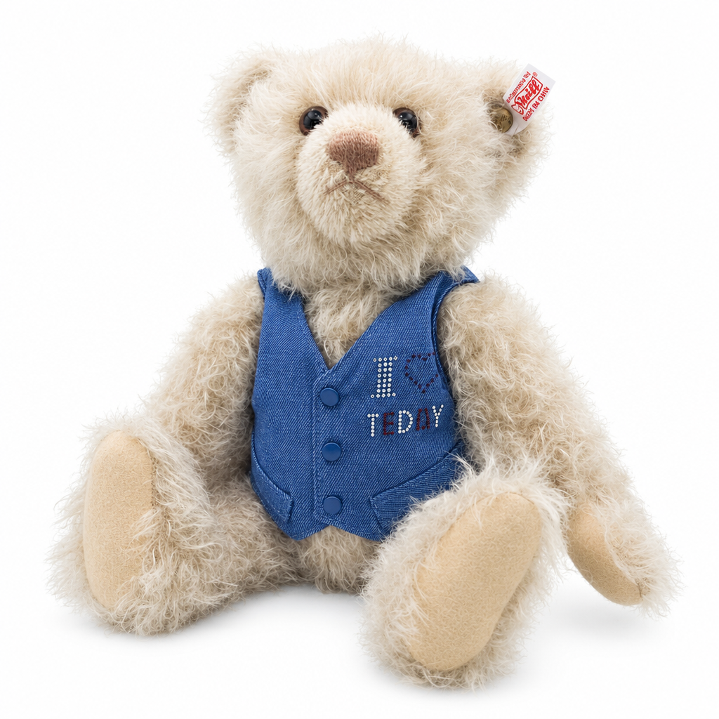 Das ist der Kristallbär, ein Teddy von Steiff. Er sitzt, hat leicht zotteliges, lockiges beiges Mohairfell mit etwas dunkler schattierter Schnauze und Augenpartie. Die Schnauze ist hellbraun und rund, die Ohreninnenseiten beige, die Pfotenballen hellbraun-beige. Die Augen sind dunkelbraun und rund, die Nase braun und dreieckig. Er trägt eine abnehmbare blaue Weste mit drei blauen Knöpfen, Strass-Schriftzug und aufgesticktem dunkelblauem Herz. Handgefertigt, voll beweglich.