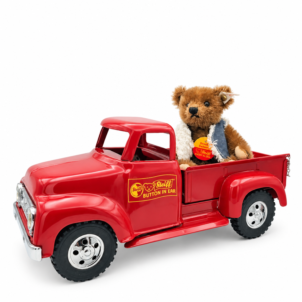 Das ist Sonderlieferung, ein Teddy von Steiff. Kleiner Mohair-Teddy mit kurzem bis mittellangem, leicht zotteligem Fell mit sanftem Schimmer. Das Fell ist braun, Schnauze, Ohreninnenseiten, Pfotenvorderseiten und Pfotenballen sind beige. Augen schwarz und rund, Nase schwarz und dreieckig. Er trägt eine blaue Jeansweste mit weißem Besatz im Sherpa-Stil und sitzt auf der Ladefläche eines roten Pick-ups. Voll beweglich, entspannte Haltung, wacher, freundlicher Ausdruck.